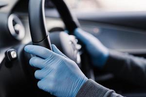 Covid-19 concept. Man drives in car, wears medical gloves, protects himself from bacteria and virus, holds car steering wheel. Coronavirus protection. Transport, quarantine and corona disease. photo