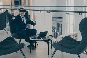 Businessman sitting in reception area of office centre during his coffee break in VR headset photo