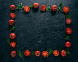 Composition of red tomatoes and green fresh parsley and dill lying on dark background in form of frame. Vegeterian food concept. Free space in middle photo