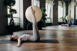 mujer joven haciendo ejercicios para las piernas con pelota de pilates mientras está acostada en la alfombra de yoga foto