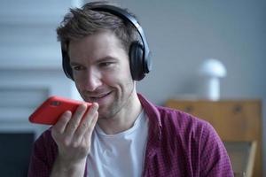 Young smiling german guy in headphones using translator app on mobile phone while studying online photo