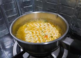 The spicy instant noodles are boiling in a metal pot on a gas stove. photo