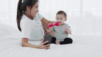 asiatisk mamma och bebis använder smartphone-selfies tillsammans på sängen, slow motion video