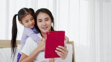Happy parent mother and cute little child daughter looking at digital tablet at home video