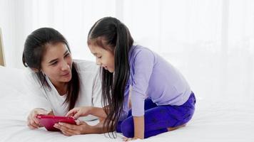 asain madre e hija pequeña leyendo libros para niños en una tableta, diviértanse en familia video