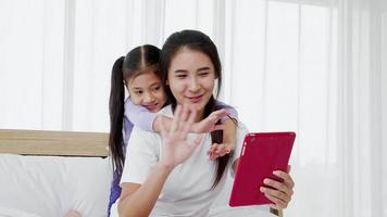 Mom playing on a tablet with a cute daughter on bed together at home