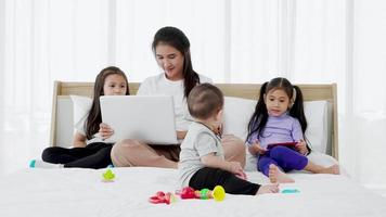 la pequeña hija y el bebé juegan juguetes de bebé juntos en la cama mientras la madre ocupada trabaja en la computadora portátil video