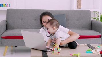 barn leker med sin mamma som arbetar hemifrån. lycklig familj hemma mamma baby video