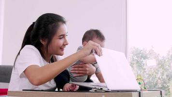 gelukkige jonge moeder met een kind dat op een computer werkt, alleenstaande moeder freelancer concept. video