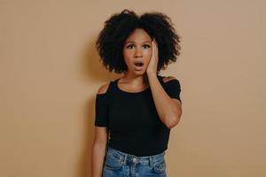 Studio portrait of young shocked african female with unexpected facial expression photo