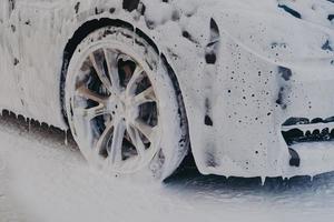 rueda de coche en espuma de jabón blanco en la estación de servicio de lavado de coches foto