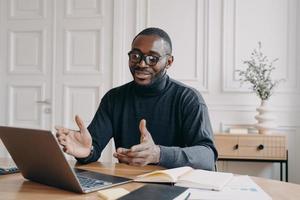 Young smiling african american businessman in glasses enjoying video call on laptop computer photo