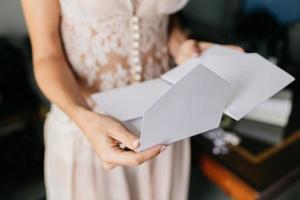 Female bride in white dress, holds white letter or envelope, prepares for invitation, prepares for wedding ceremony. Marriage concept photo