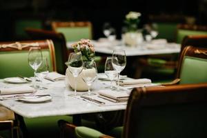 Horizontal shot of square table served with empty glasses, napkins, plates, forks and knives with no dish, green chairs around. Cozy restaurant or cafe photo