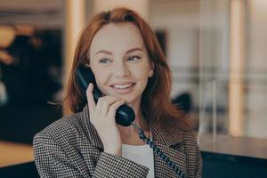 retrato de una trabajadora de oficina satisfecha usando un teléfono fijo negro, llamando a un socio comercial foto