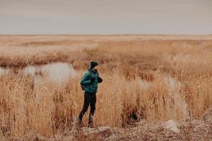 foto lateral de un hombre atractivo vestido con sombrero, chaqueta y pantalones de moda, lleva mochila, se para al aire libre, tiene un viaje inolvidable, disfruta del tiempo de otoño. concepto de personas, descanso y estilo de vida