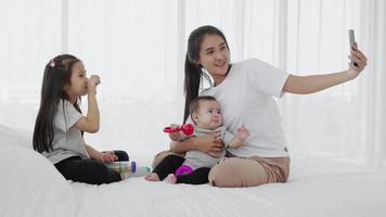 mother, daughter, baby use smartphone selfies together on bed, Slow motion video