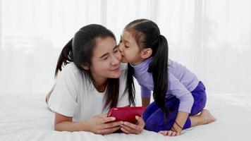 daughter kisses her mother while use tablet on bed, happy single mom concept video