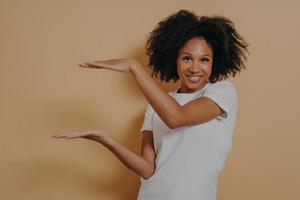 Young dark skinned showing large object, shaping box with both hands, isolated over beige background photo