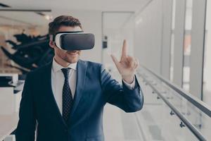 Smiling business professional in suit wearing VR headset on head using virtual reality at workplace photo