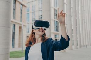 una alegre pelirroja vestida formalmente se encuentra al aire libre con gafas de realidad virtual foto