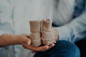 Unrecognizable woman and man anticipate for baby holds small booties. Family motherhood fatherhood concept. Future parents. Birth photo