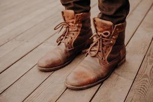 Top view of mans shoes on wooden floor or surface. Old footwear. Unrecognizable man. Leather shaggy brown boots with laces photo