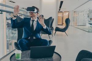 Exited CEO in VR headset enthusiastically testing app on laptop sitting in business centre lobby photo