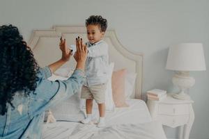 Cute happy small afro american kid playing with his mom in bedroom at home photo