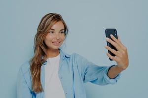 Beautiful woman taking photo of herself on light blue background