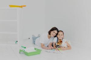 miembros alegres de la familia con perro yacen en el suelo en una habitación vacía que necesita mejoras, eligen el color en la muestra de la paleta, terminan la redecoración de la casa, tienen una buena relación. trabajo en equipo, tareas de la casa foto