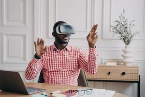 Concentrated Afro american businessman using VR headset, experiencing virtual reality playing game photo