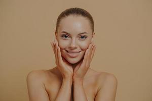 Young beautiful woman with bare shoulders touching cheeks, enjoying her soft and smooth skin photo