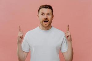 Excited young man pointing with two forefingers up and with shocked face expression photo
