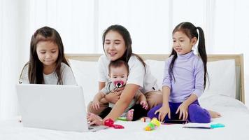 Busy single mom concept, mother working on laptop and caring for her baby and little daughte video