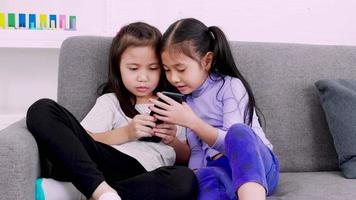 Two happy cute little girls using smartphone for playing or studying together at home