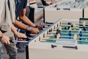 Two men stand on one side, play table football together, enjoy heat games, like kicker, spend free time outdoor. Team and companionship concept photo