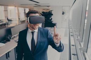 Young businessman in elegant suit using VR headset, touching exploring virtual reality at work photo