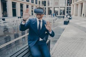 Handsome businessman sitting outside on bench while wearing portable Virtual Reality glasses photo