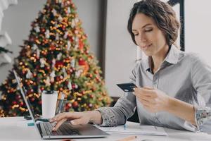compras navideñas en línea, joven italiana con tarjeta de crédito de plástico y escribiendo en una laptop foto