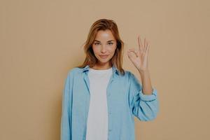 Young lady expressing approval with okay gesture on beige background photo