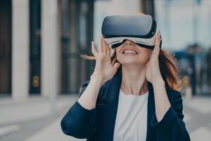 Amazed red haired female office worker being excited while trying out VR glasses outdoors photo