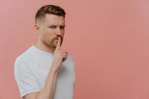 Young bearded serious man showing gesture of silence photo