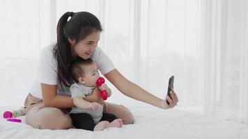 mamma ta hand om sin baby medan du använder smartphone för att ringa på sängen, slow motion video