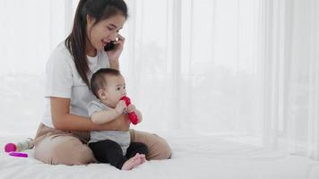 feliz madre asiática y bebé recién nacido sentados y usando un teléfono inteligente video