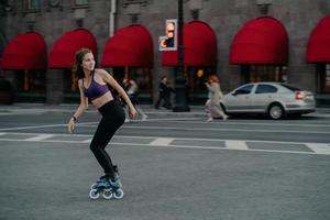 Full length shot of active slim young woman dressed in sportsclothes rides on rollers to strengthen arms and legs muscles improves balance agility and coordination has good mood burns calories photo