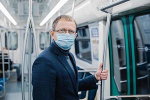 una foto de un joven usa gafas y una máscara protectora para evitar la propagación de la enfermedad del coronavirus o la epidemia de gripe en el transporte público, posa en un vagón de metro vacío. solución de salud pública