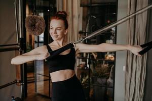 alegre joven instructora de pilates haciendo ejercicio de fuerza manual en reformador foto