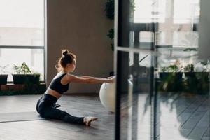 Young redhead slender woman sitting in twine with fitball, doing stretching exercises photo