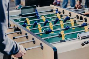 Cropped image of active people play kicker or table football, want to achieve success and win, prefer sport games. Soccer table with yellow and blue plastic players photo
